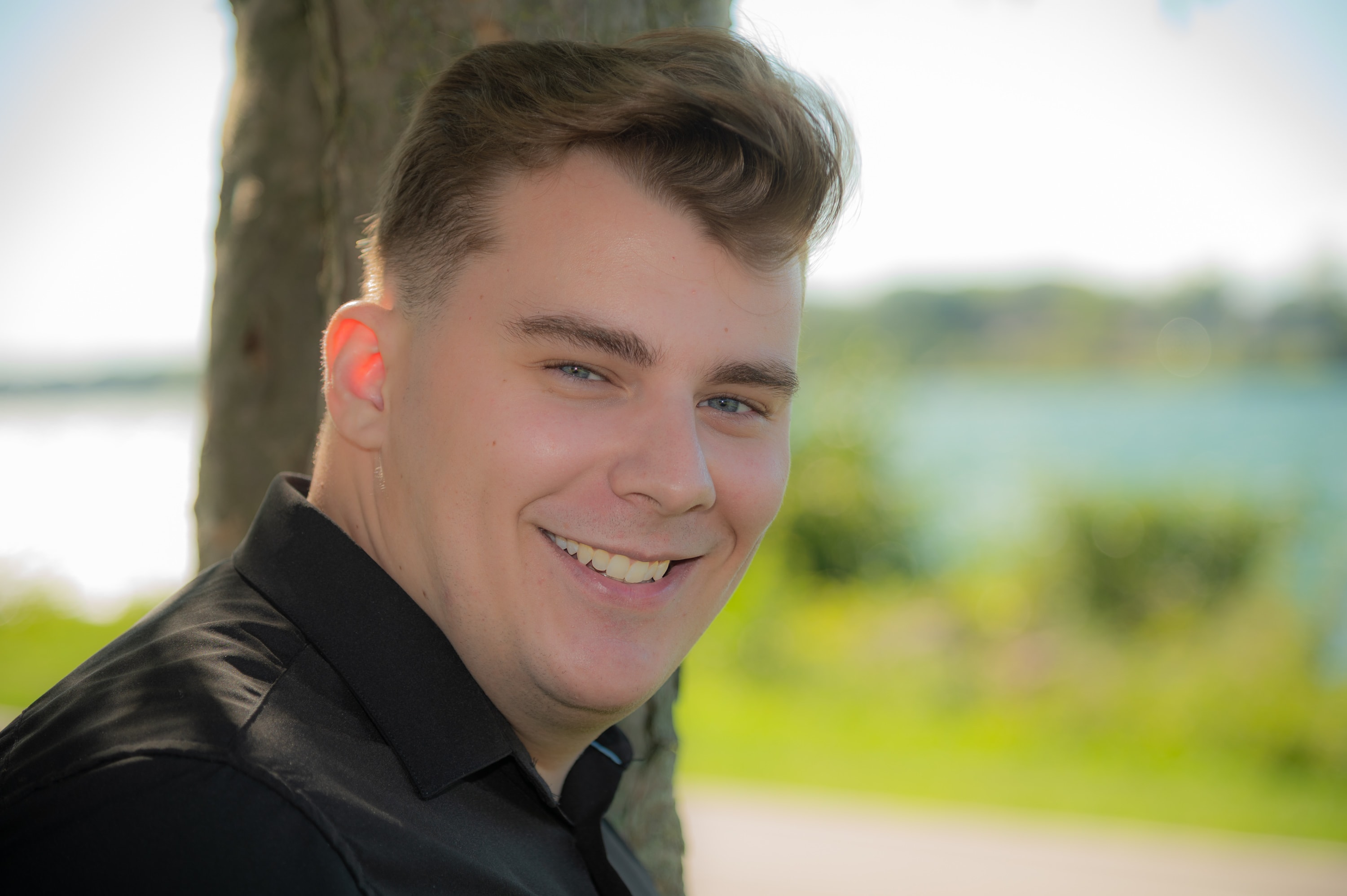 Young man smiling outdoors by tree