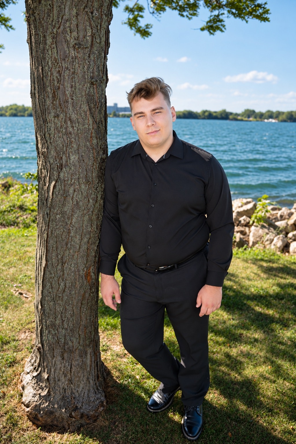 Young man in black shirt leaning against tree by the water