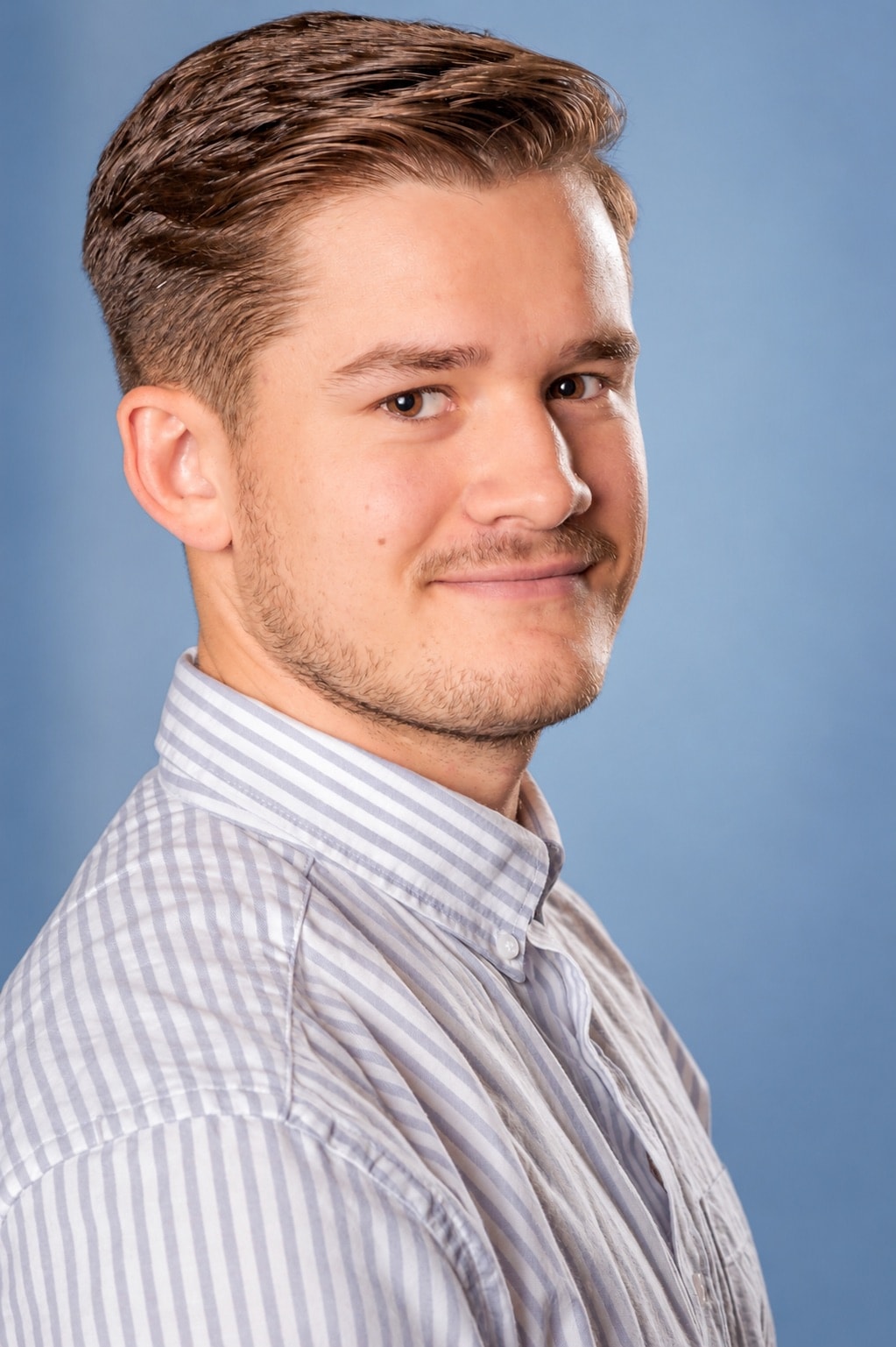 Professional headshot of young man against blue background